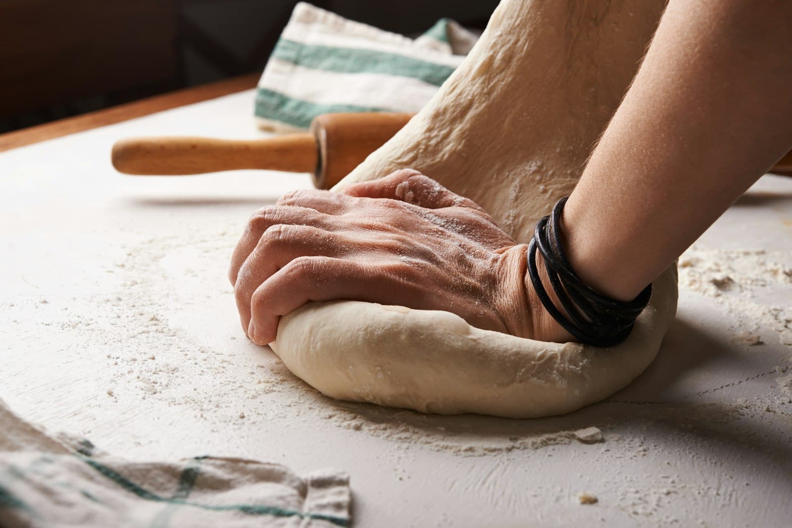 A baker shaping dough by hand beside a wooden rolling pin